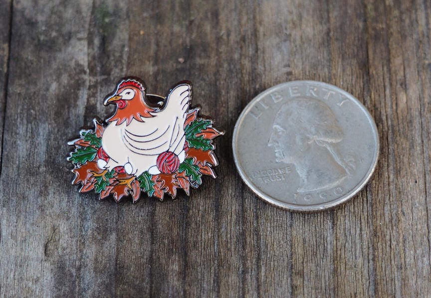 An enamel pin of a chicken next to a quarter for comparison. 