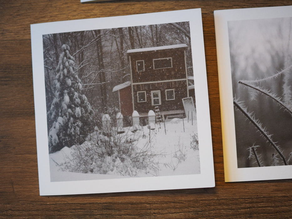 A note card with a photo of a snow covered garden with a red cabin in the background.