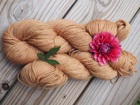 two skeins of coppery colored yarn with a pink dahlia on top.