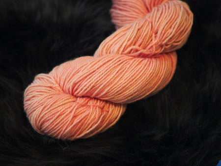 one skein of coppery pink yarn sitting on a black background