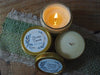 Three candles sit on a green woven fabric. Two are open, one is lit. The label says "Chocolate Cupcake Lotion Candle"